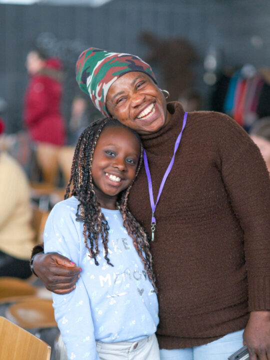 A woman embraces a young girl as they both smile at the camera