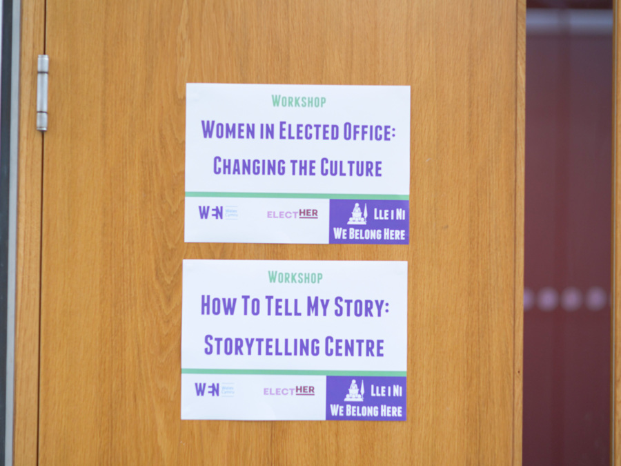Two posters on a door, advertising the workshops taking place in that room. The first reads 'Women in elected office: changing the culture'. The second reads 'How to tell my story: Storytelling centre.'