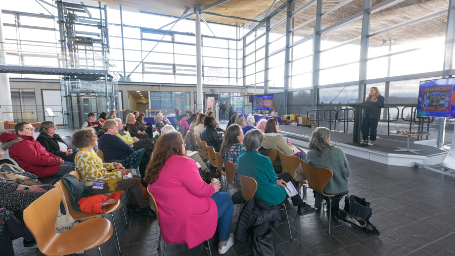 An audience sit in the Neuadd of the Senedd listening to a workshop facilitated by Sarah Rees, who is on stage
